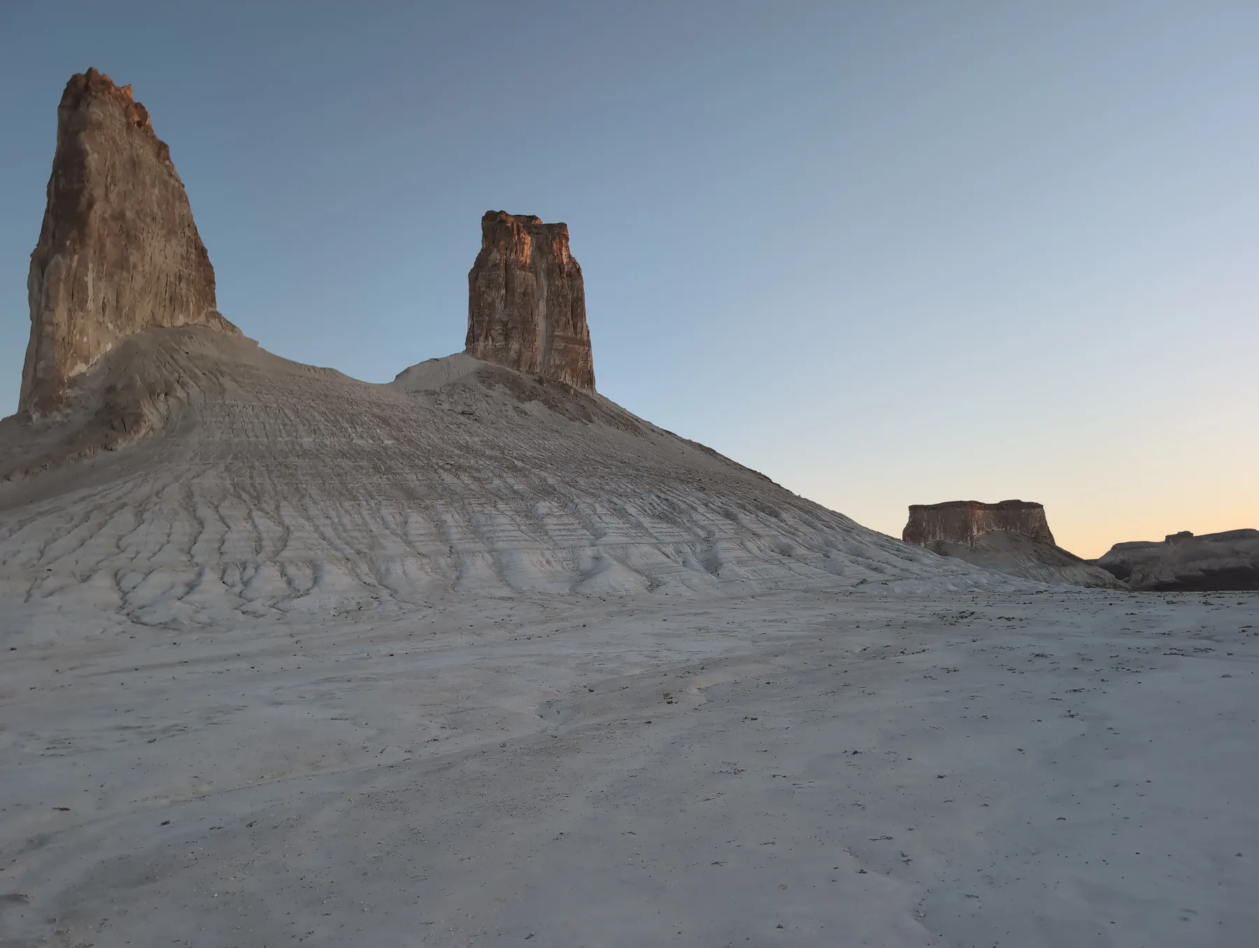 A white chalk fang and a row of conical peaks below a plateau rim, seen from a cliff edge.